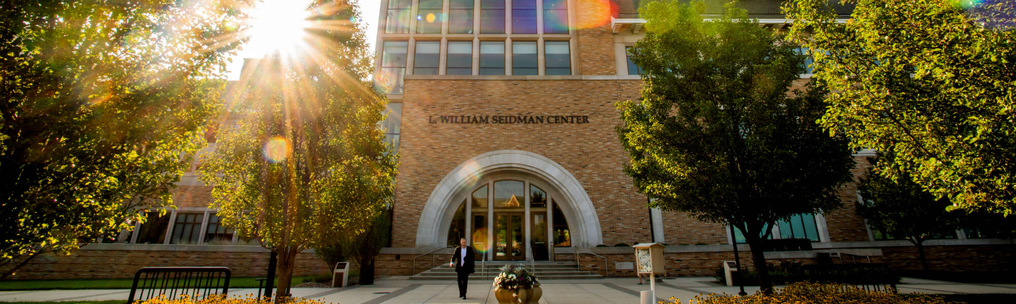 Seidman College of Business exterior with the sun rising between the trees